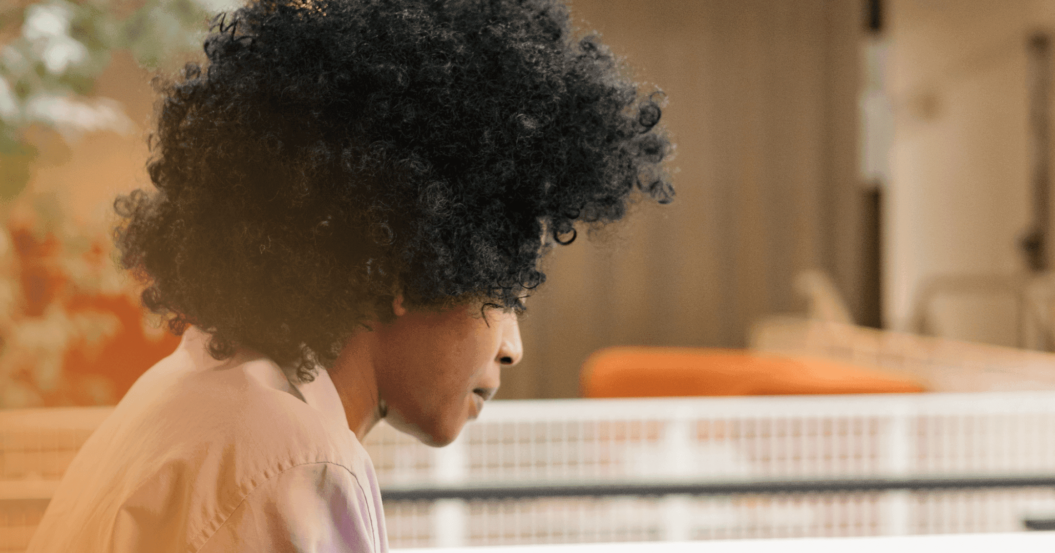 Woman sits in a chair, looking down at something in front of her. Her facial expression isn't visible. There is a gate behind her.