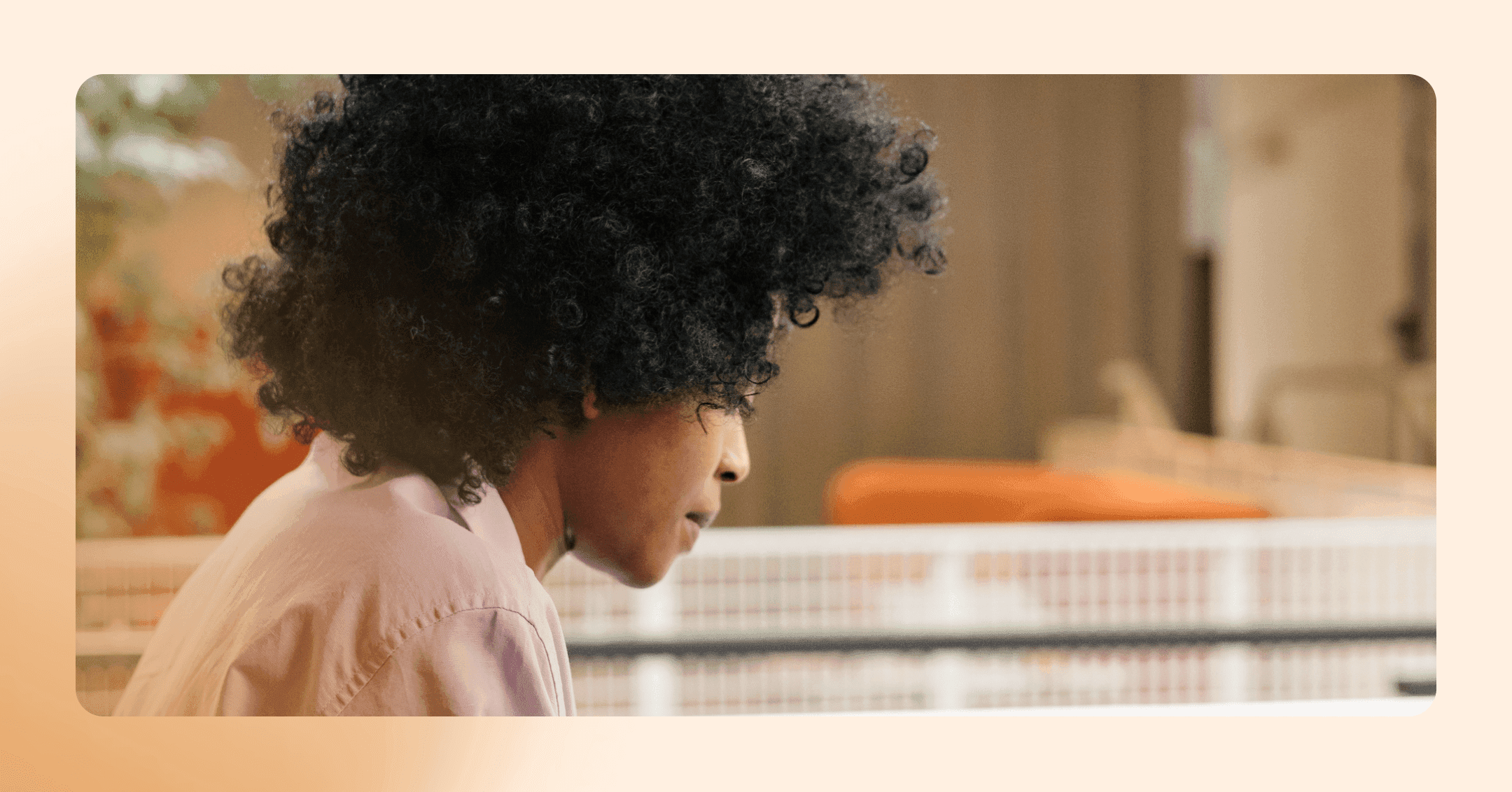 A woman with black, curly hair looks down off camera. She is in an open layout office space.