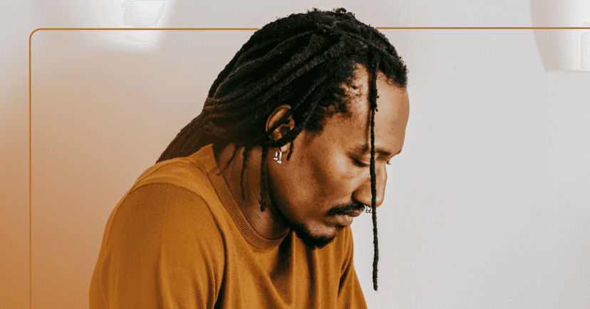 Man with dreadlocks and a brown shirt looking down and to the right. He has a sad face. The image is framed in brown.