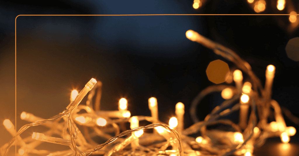 Image shows strings of lit white holiday lights. They are sharp in the foreground then the lights get blurry as it fades into the background. The background is black.