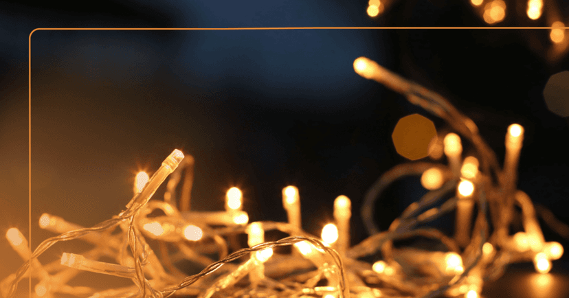 Image shows strings of lit white holiday lights. They are sharp in the foreground then the lights get blurry as it fades into the background. The background is black.