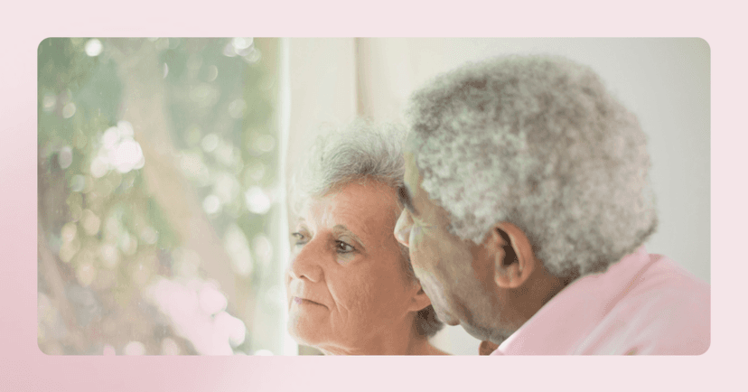 An older couple looks out a window with serious faces. Out the window is a tree. The image is framed in a pink color.